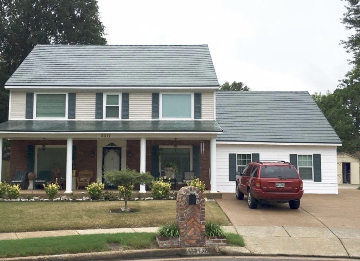 Two-story beige house with a red SUV in the driveway, mailbox and a green lawn.