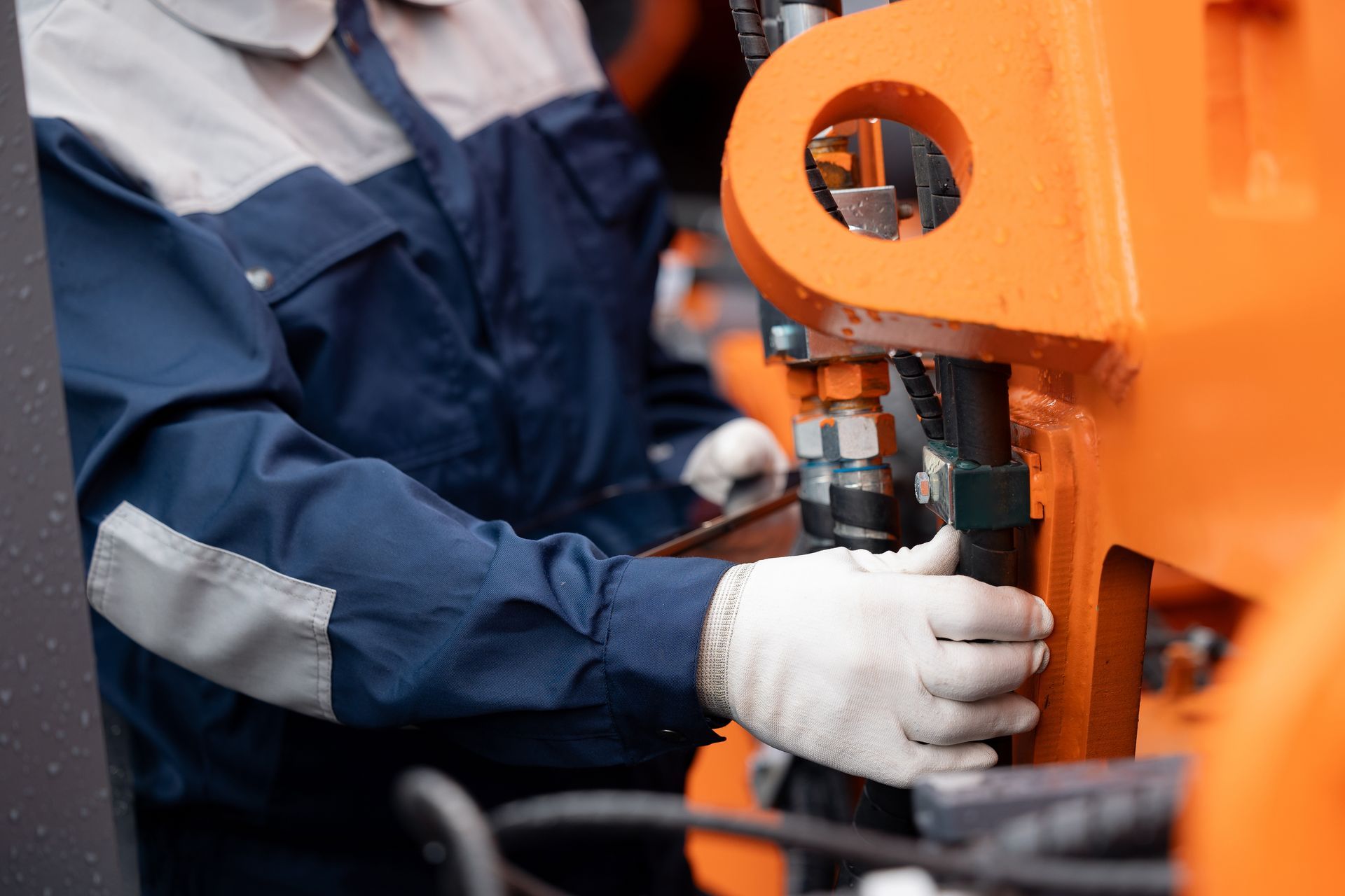 Worker in blue coveralls and white gloves operating an orange industrial machine