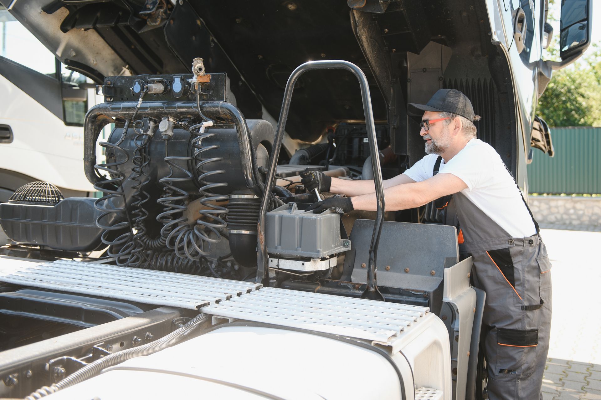 Technician in white shirt works on exposed truck engine under raised cab.