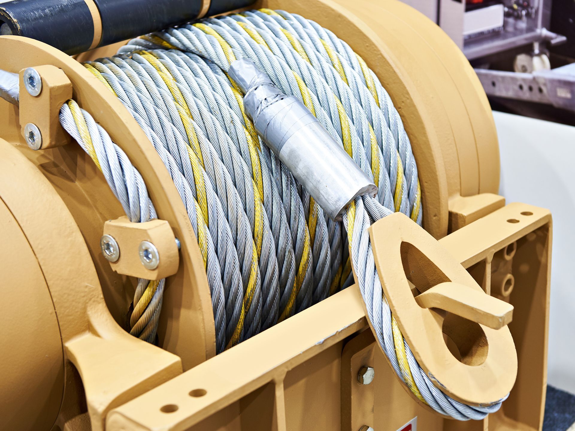 Yellow industrial winch with tightly wound steel cable and metal hook assembly