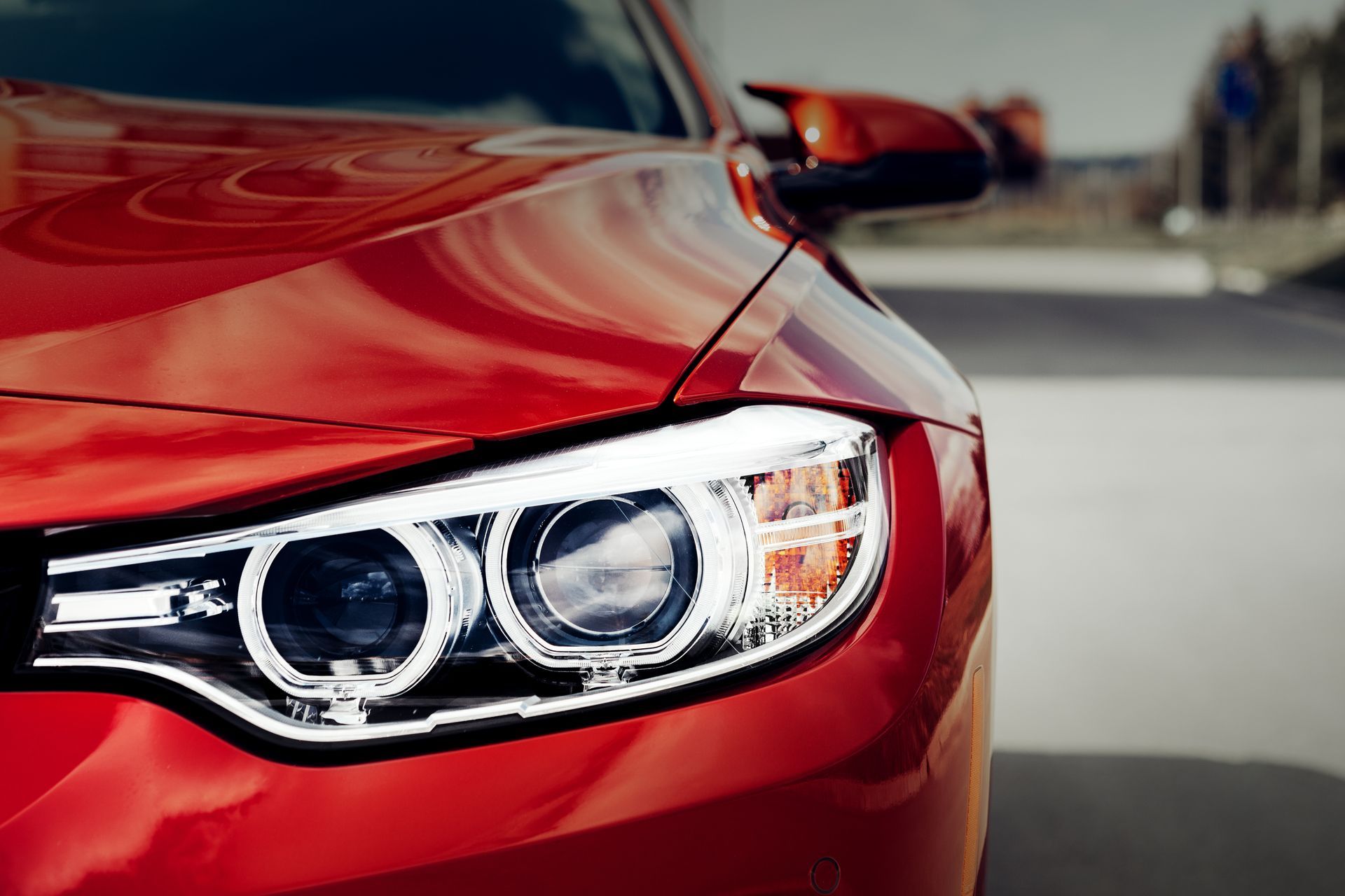 Close-up of a red car’s front headlight and hood on a road