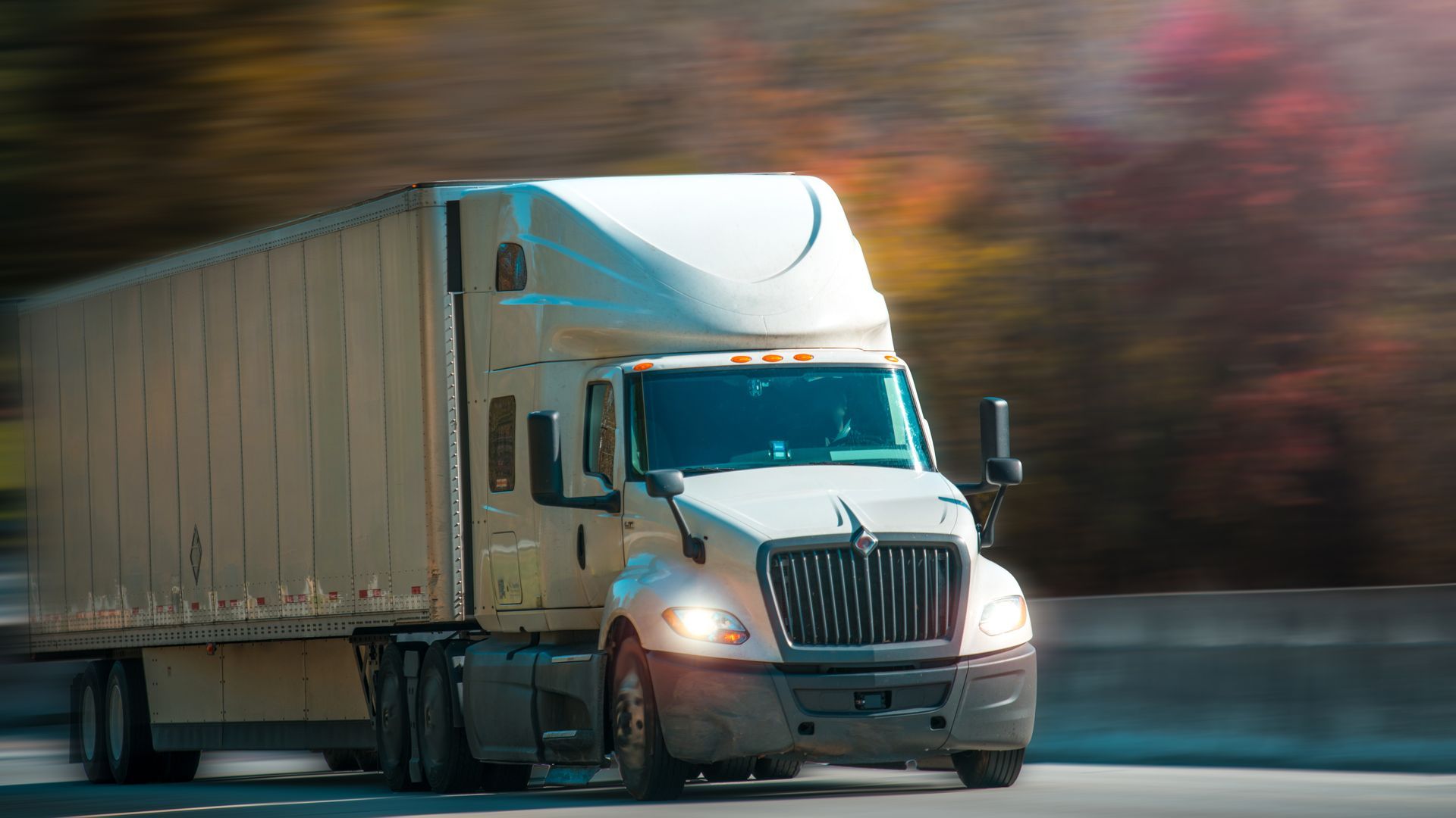 White semi-truck driving on a highway with blurred trees in the background