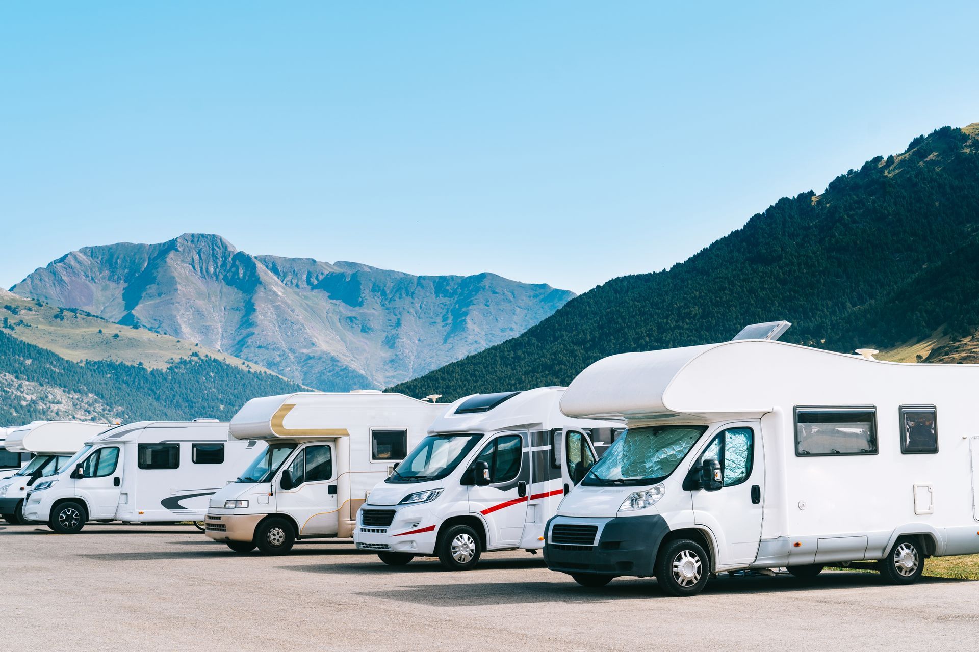 Row of parked white camper vans and motorhomes in a mountain lot under a clear blue sky