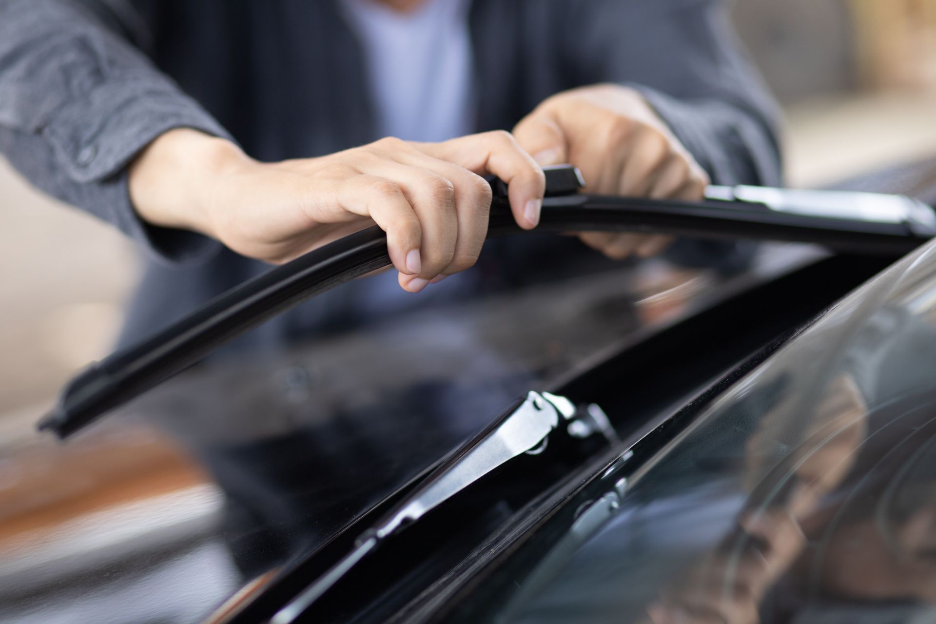 Hands replacing a windshield wiper on a car in a garage