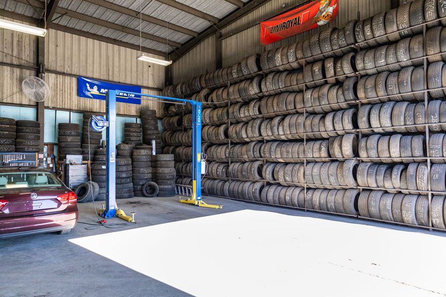 Warehouse interior stacked with rows of tires and a red car parked under blue lifting equipment
