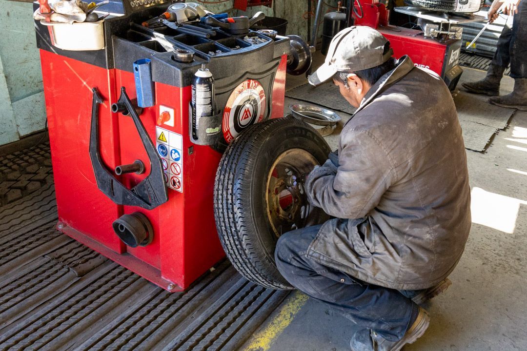 Mechanic kneeling beside a red tire balancing machine in a workshop, adjusting a car tire