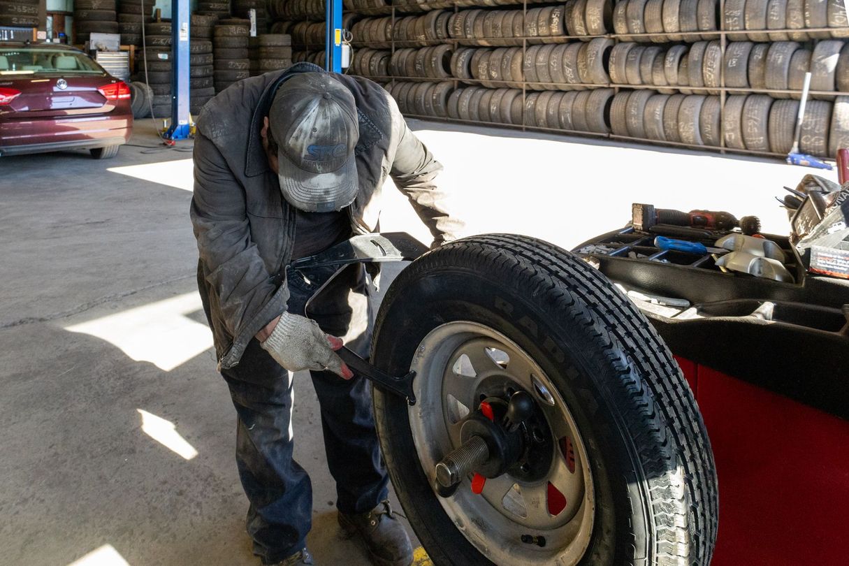 Mechanic inspecting a tire on a car in a garage, with stacked tires in the background