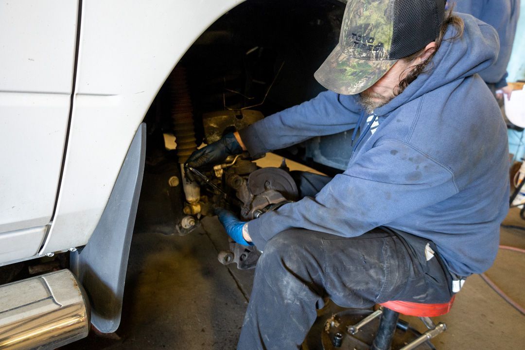 Mechanic working on a car’s wheel well with tools in a garage