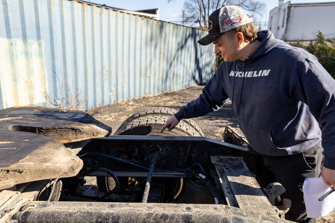 Worker in a cap inspecting a charred metal container beside a shipping container outdoors