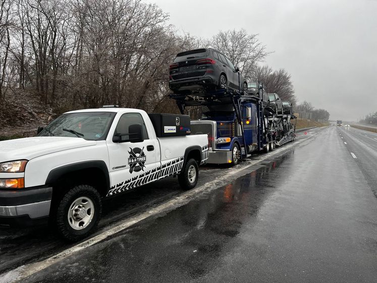 Tow truck hauling a black SUV on a wet roadside under overcast skies