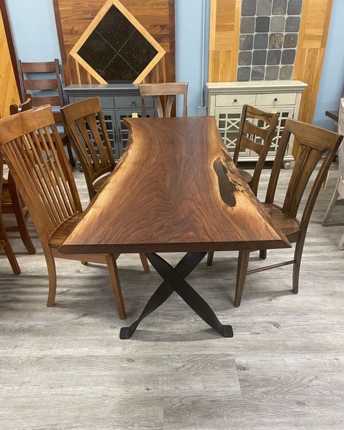 Wooden dining table with black metal base, surrounded by chairs in a rustic indoor setting