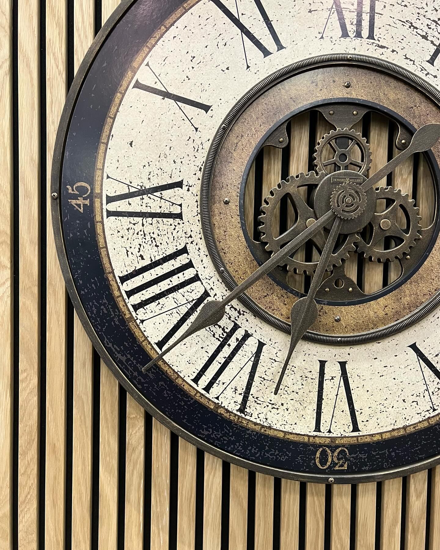 Vintage clock face with Roman numerals and exposed gears on a striped wall