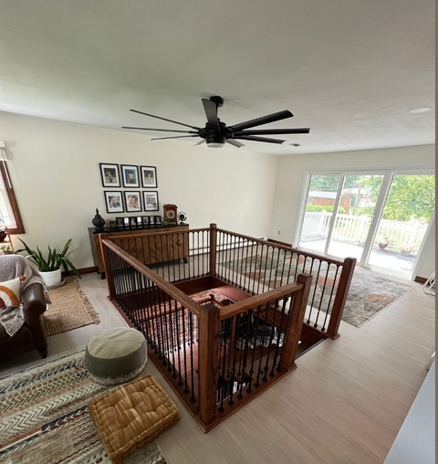 Bright living room with a staircase railing, black ceiling fan, and sliding glass doors to a patio.
