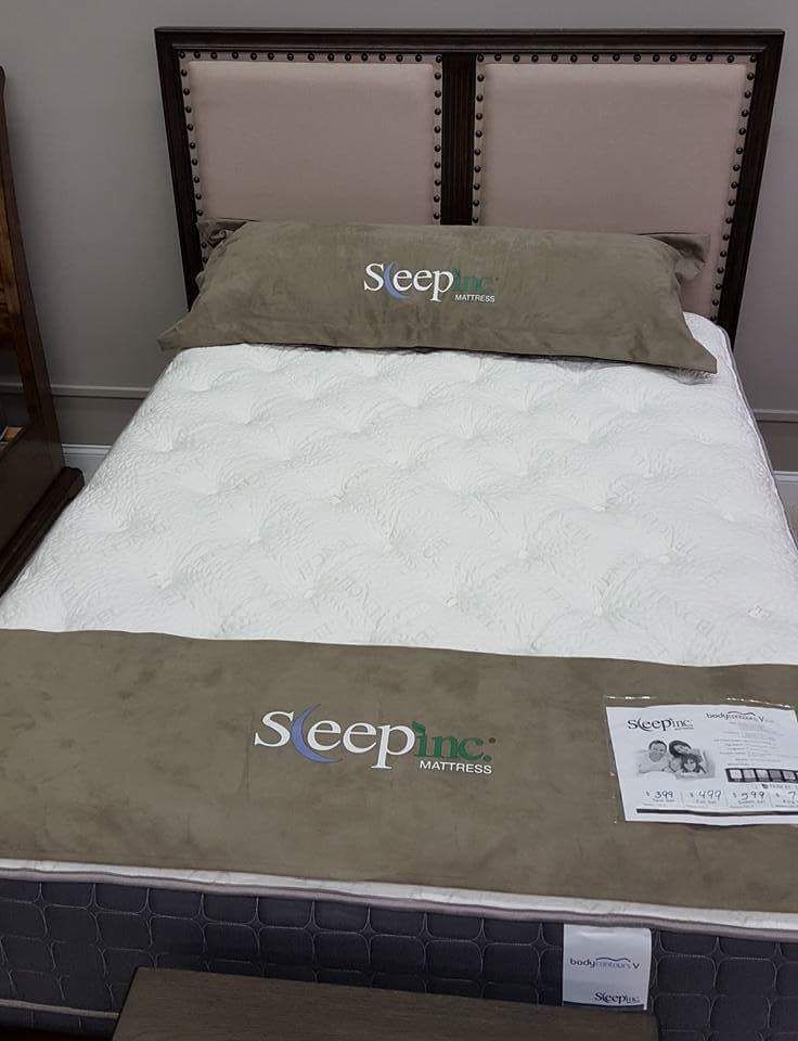 Mattress display with white quilted top, olive cushions, and brown upholstered headboard in a store.