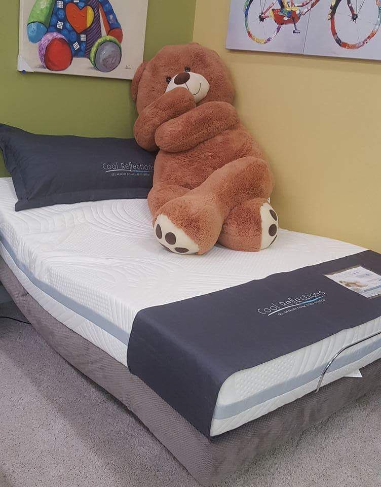 A teddy bear propped on a neatly made single bed with dark blue bedding in a bedroom.