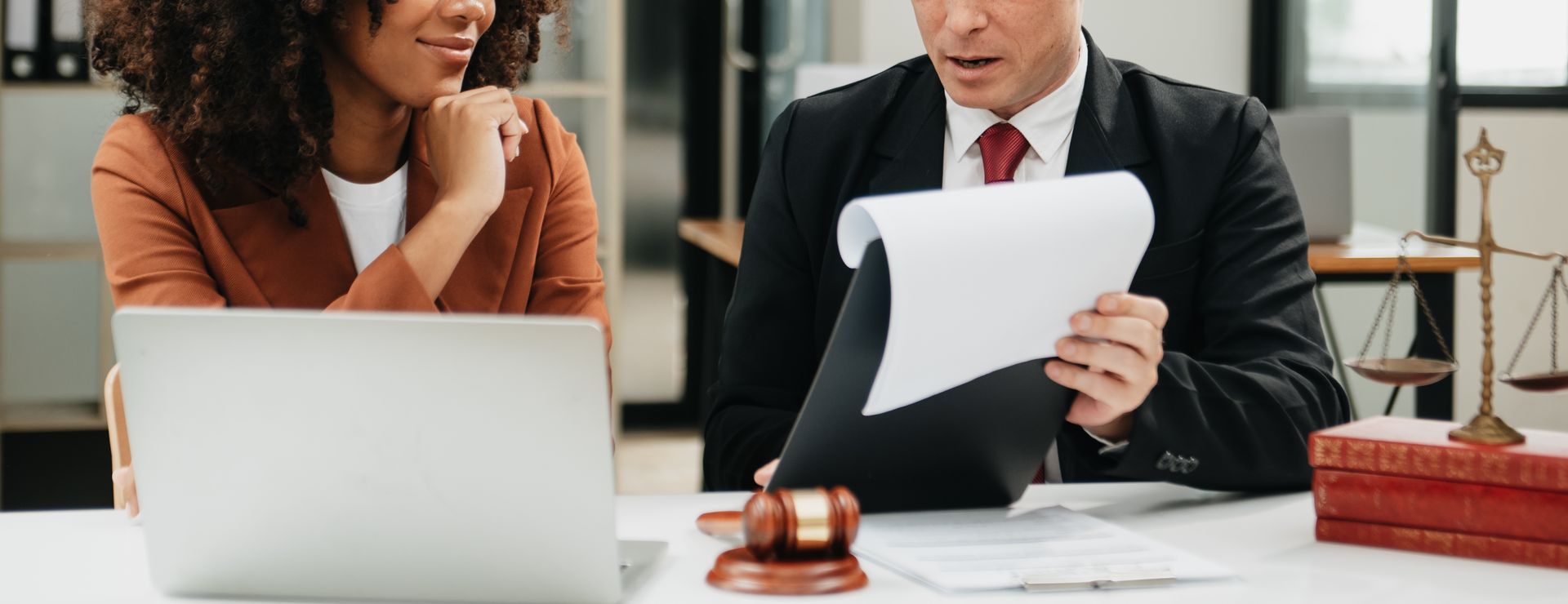 Two people reviewing documents at a desk with a laptop and gavel in a legal office