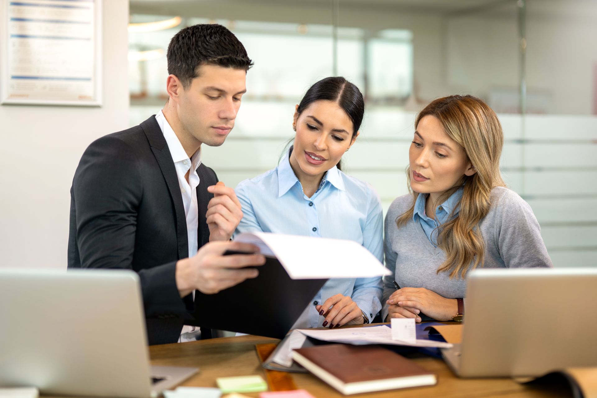 Three coworkers review a document together at a desk in a bright office.