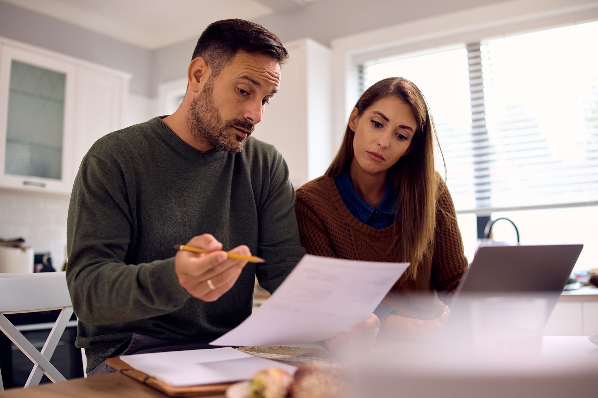 Two people review documents at a table beside a laptop in a bright office.