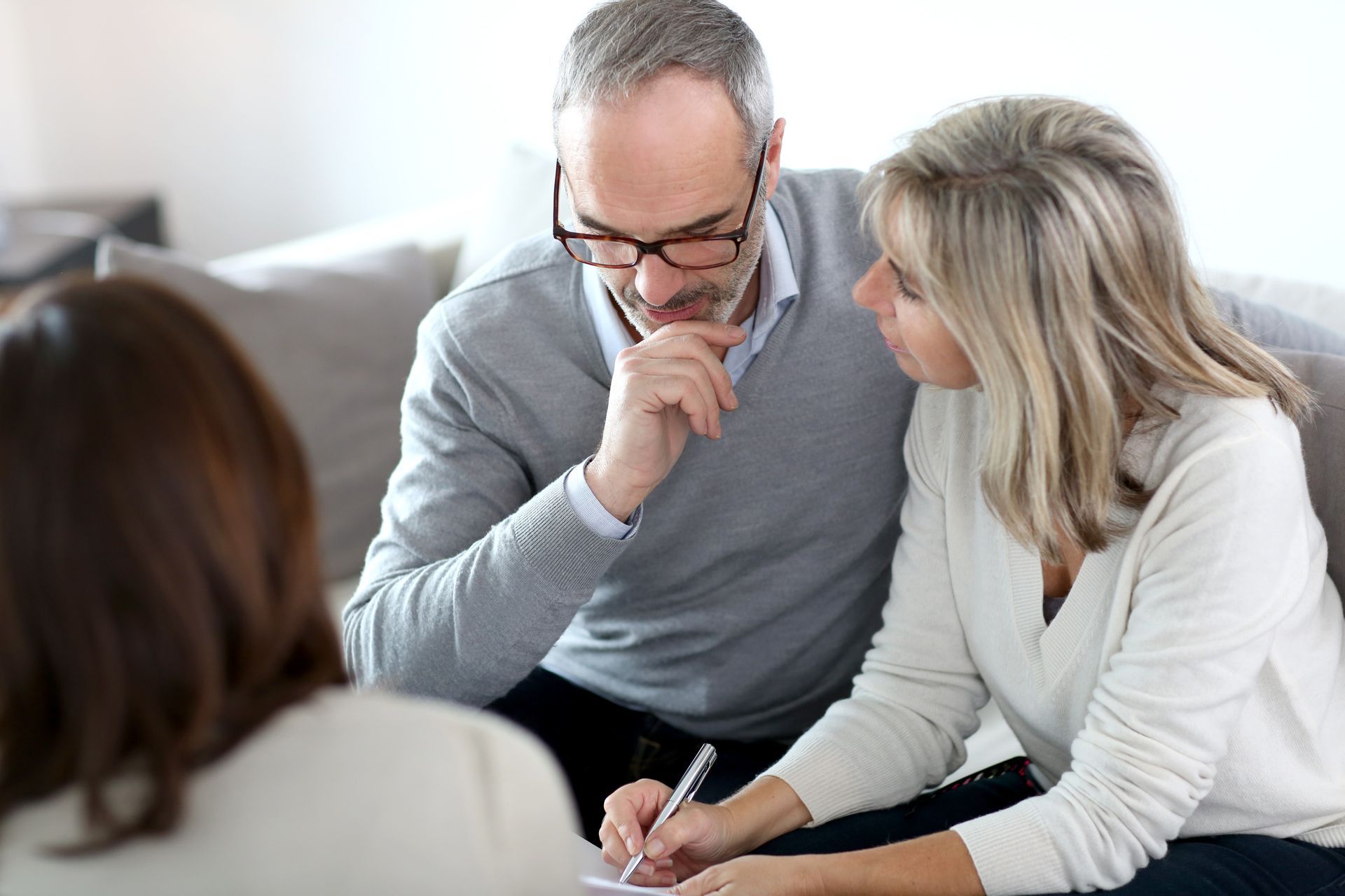 Three people in a bright room discussing paperwork, with two leaning over documents on a couch