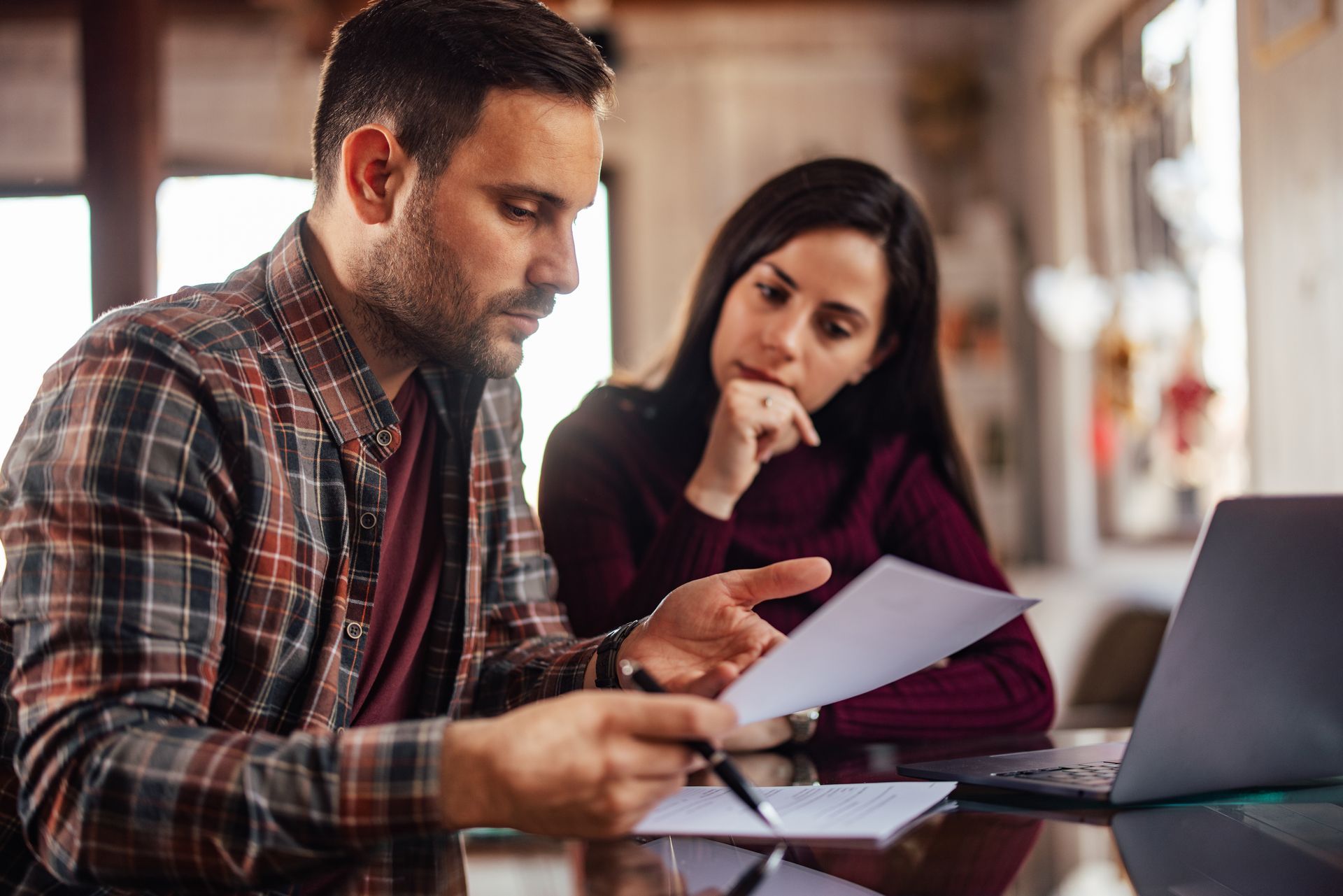 Two coworkers reviewing documents at a table beside a laptop in a bright office