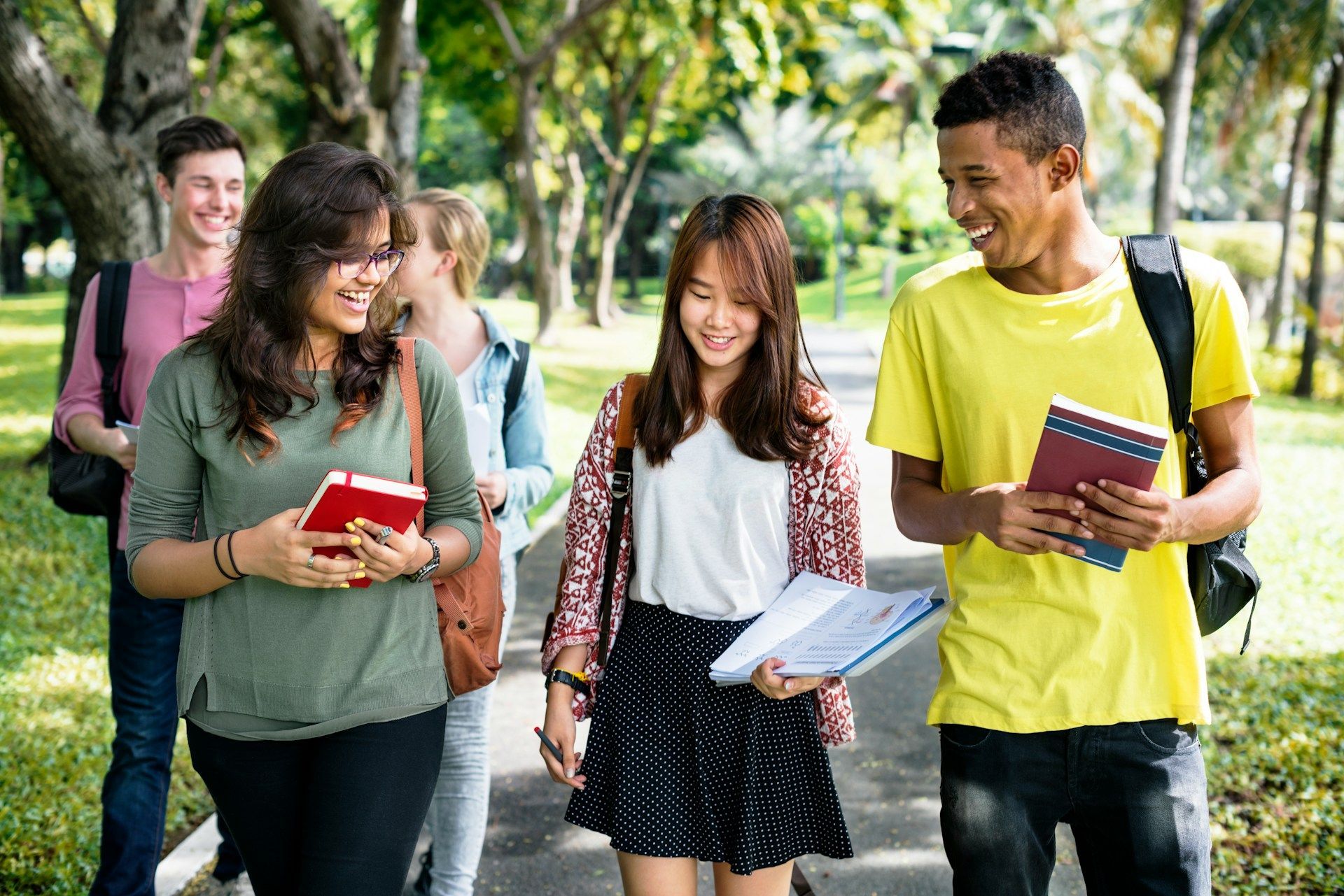 Students walking together outdoors on a sunny campus, smiling and carrying books.