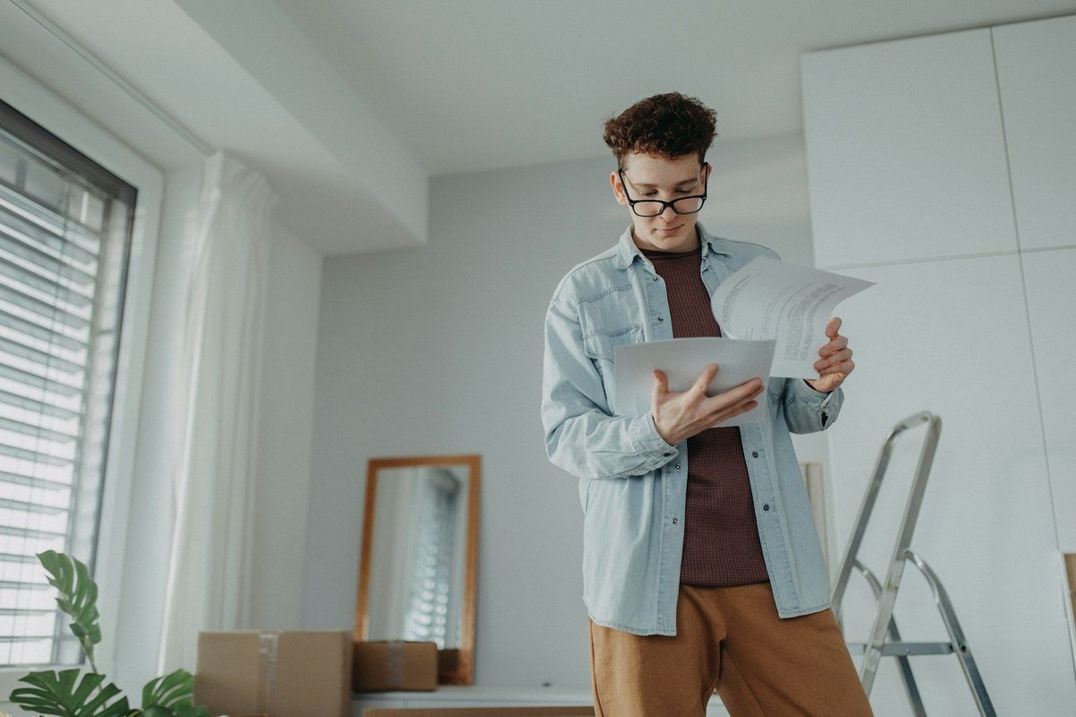 Person reading papers in a bright room beside a ladder and window.