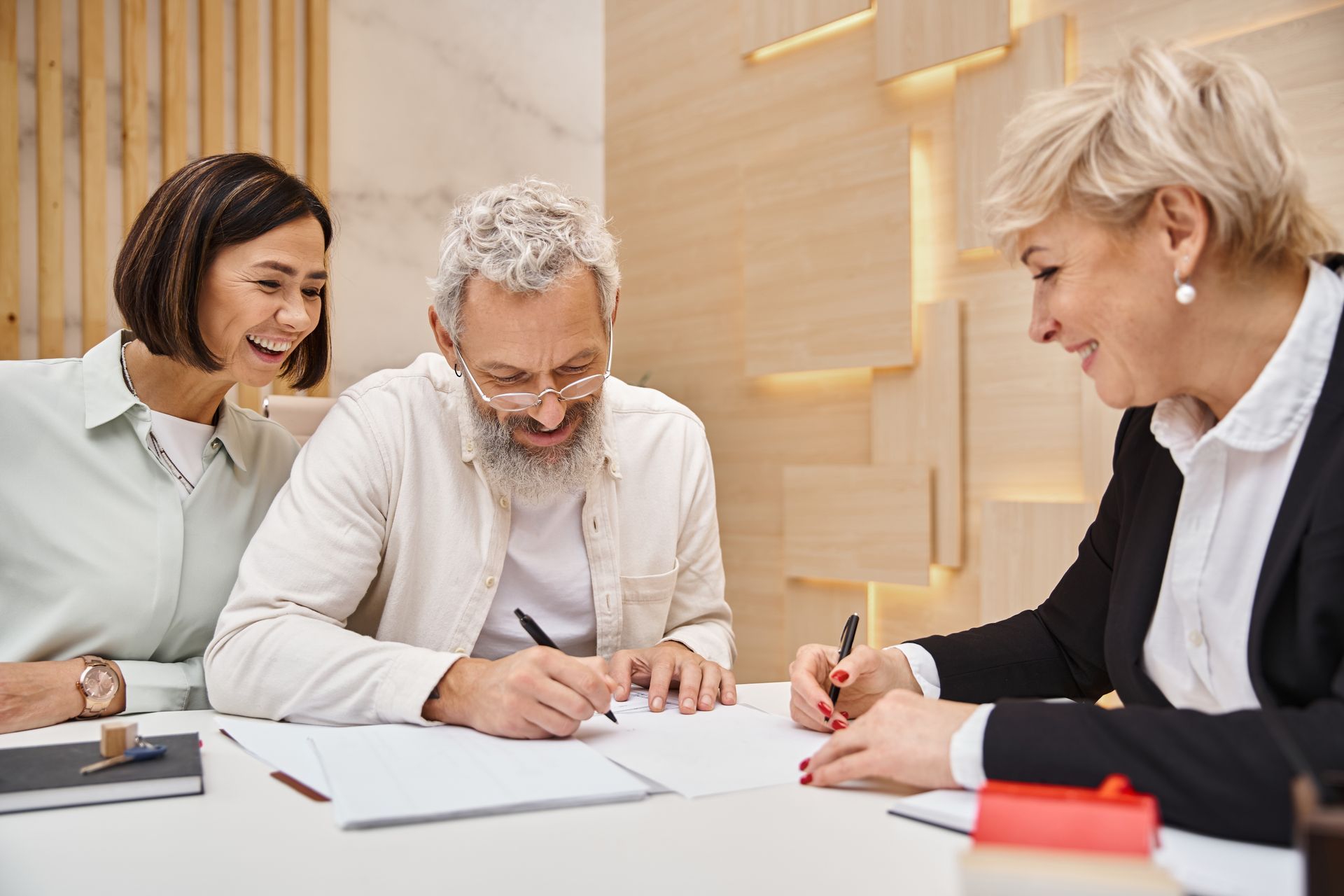 Three coworkers smiling and signing documents at a bright office table