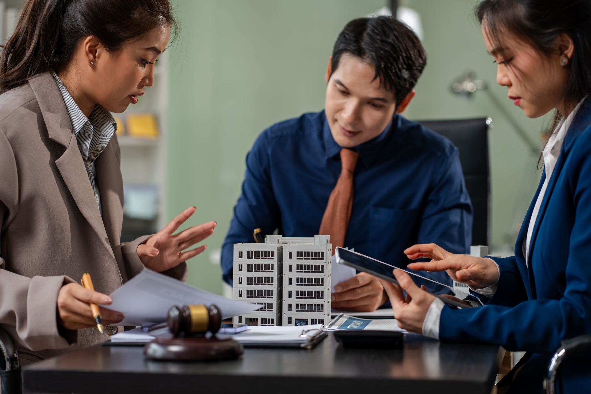 Three people reviewing a building model and documents at a meeting table