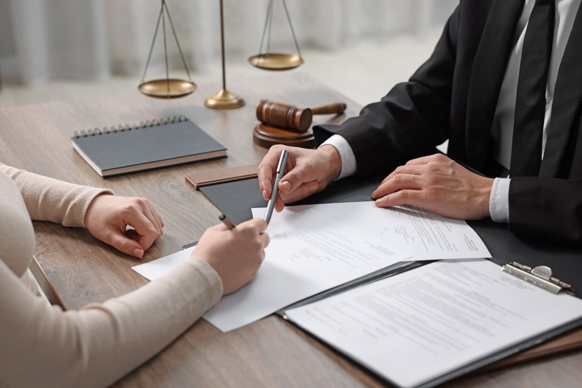 Two people signing legal documents at a desk with a gavel and scales of justice nearby