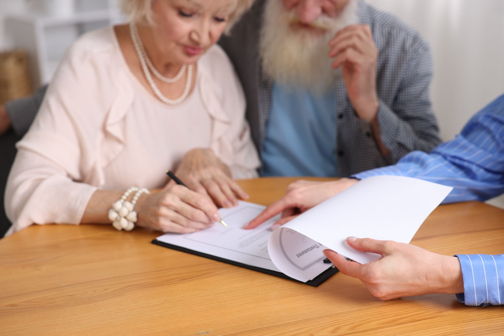 Two people signing documents at a wooden table, with a third person holding papers nearby