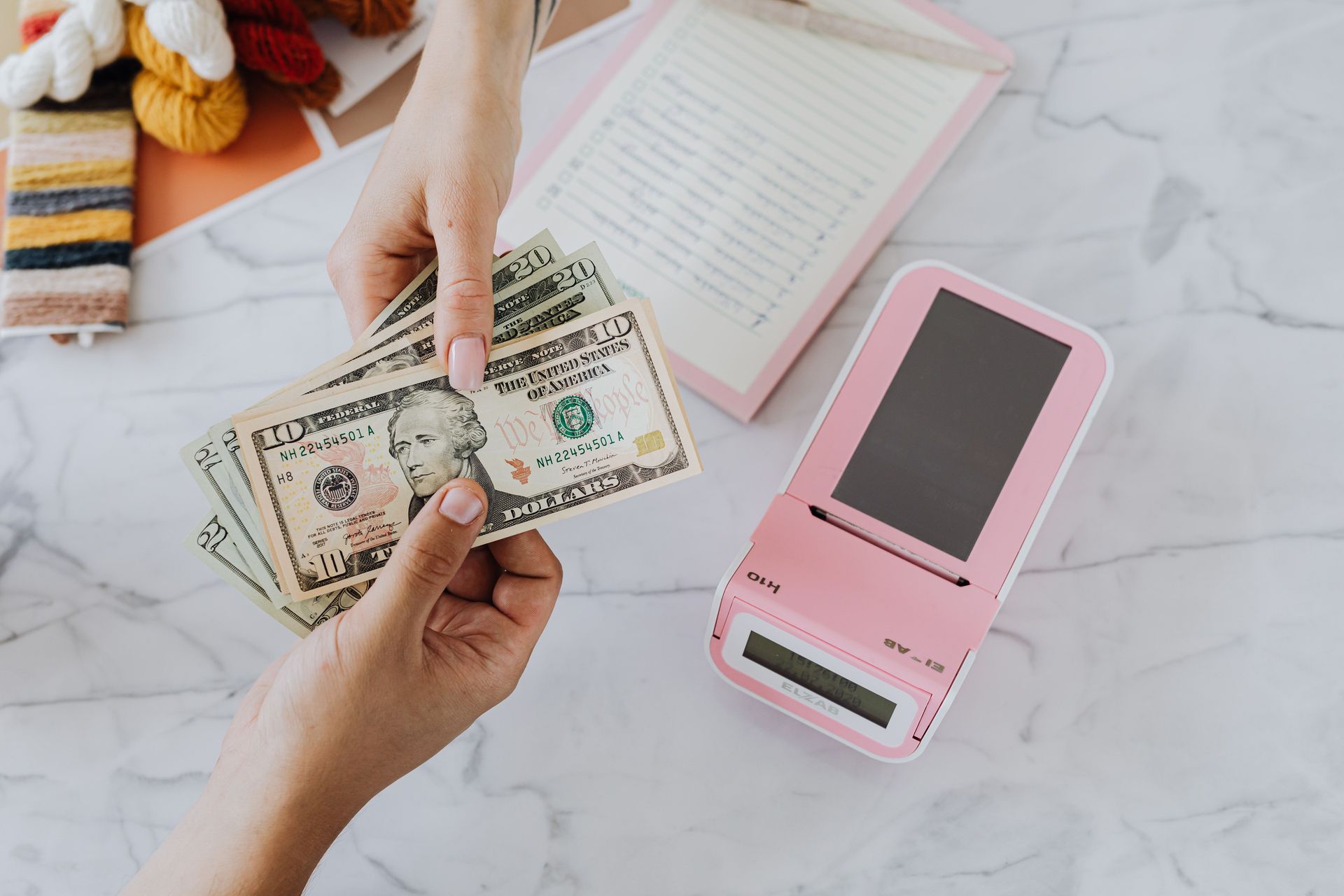 Hands exchanging cash beside a pink card reader on a marble table