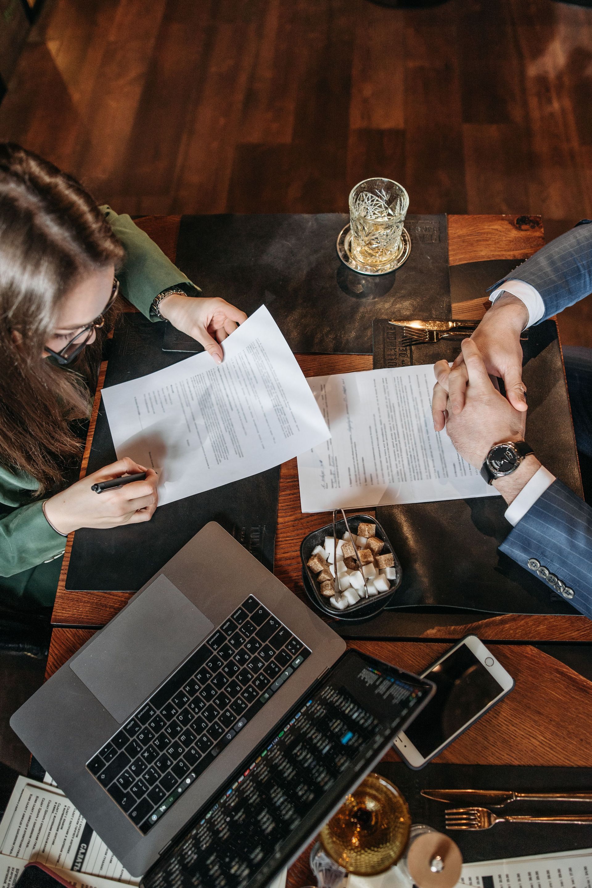 People reviewing documents around a laptop and coffee on a wooden table, top-down view