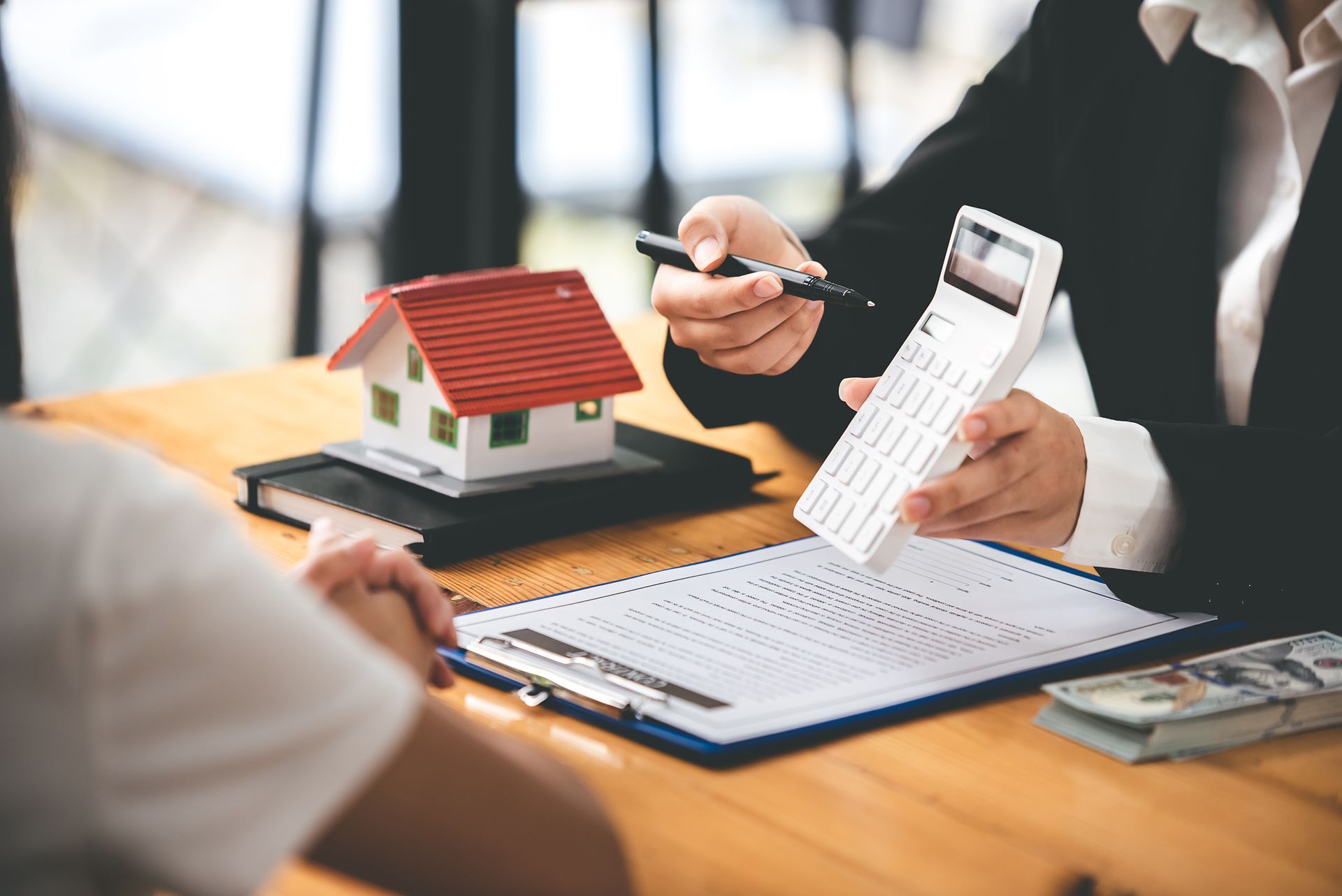 Person reviewing house model and calculator with paperwork at a desk