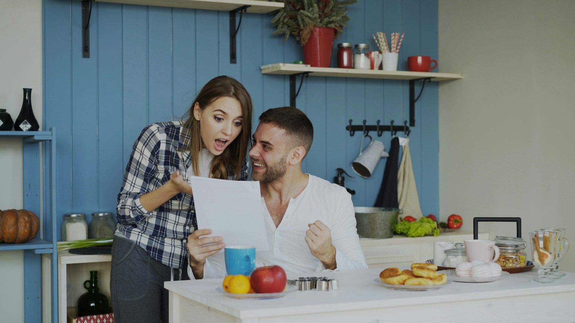 Two people in a blue kitchen reviewing a recipe sheet while preparing ingredients on the counter.