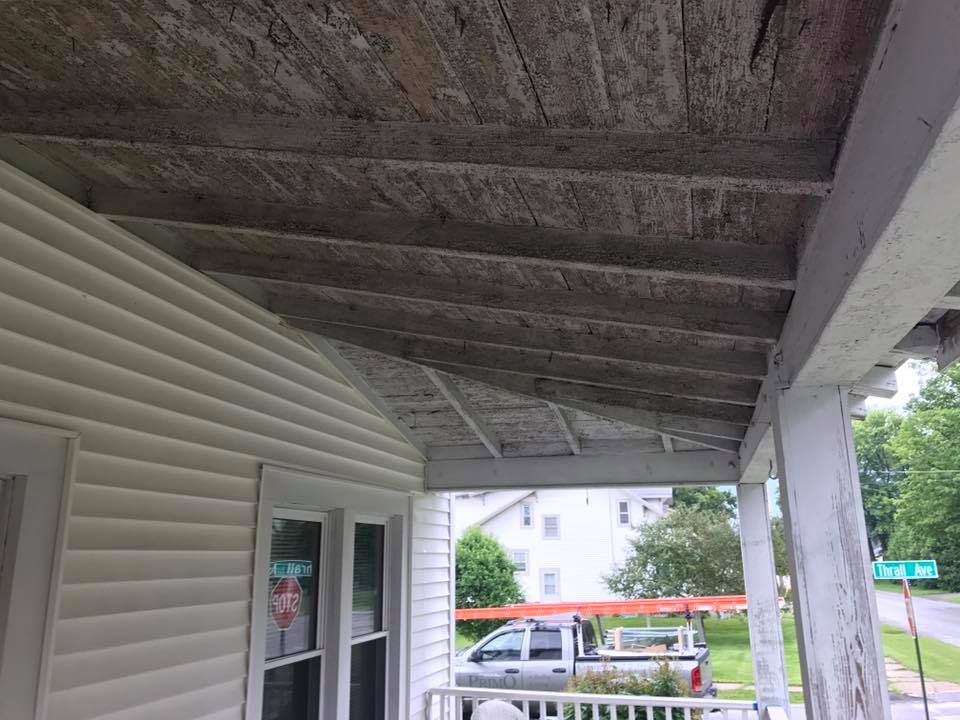 a porch with a wooden ceiling and a white house in the background .