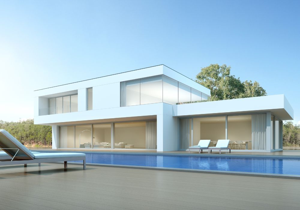Une maison moderne, blanche et élégante, dotée de grandes fenêtres, donne sur une piscine rectangulaire agrémentée de chaises longues sur la terrasse.
