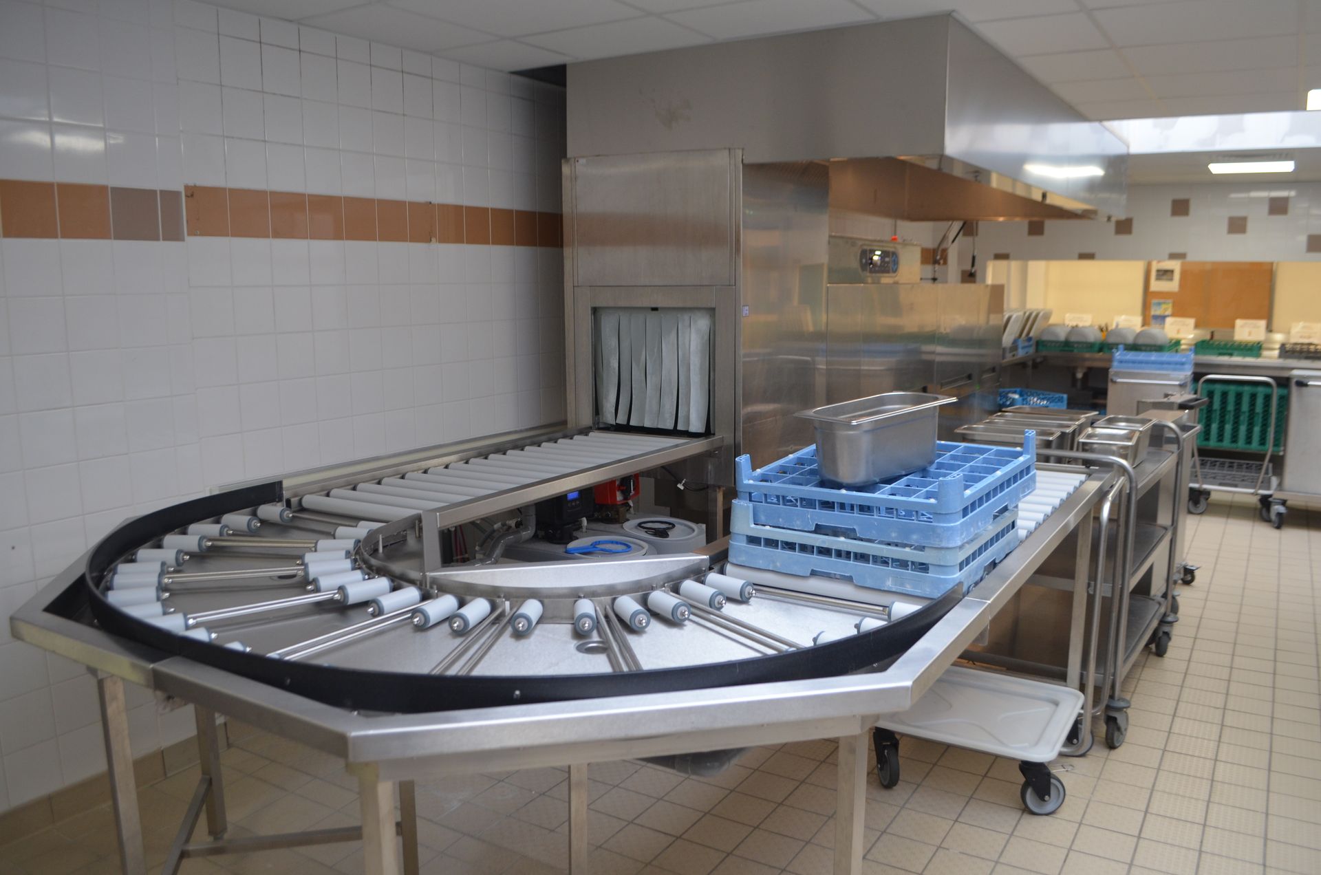 Zone de cuisine commerciale équipée d'un système de convoyeur en acier inoxydable pour le transport des casiers à vaisselle vers un lave-vaisselle.