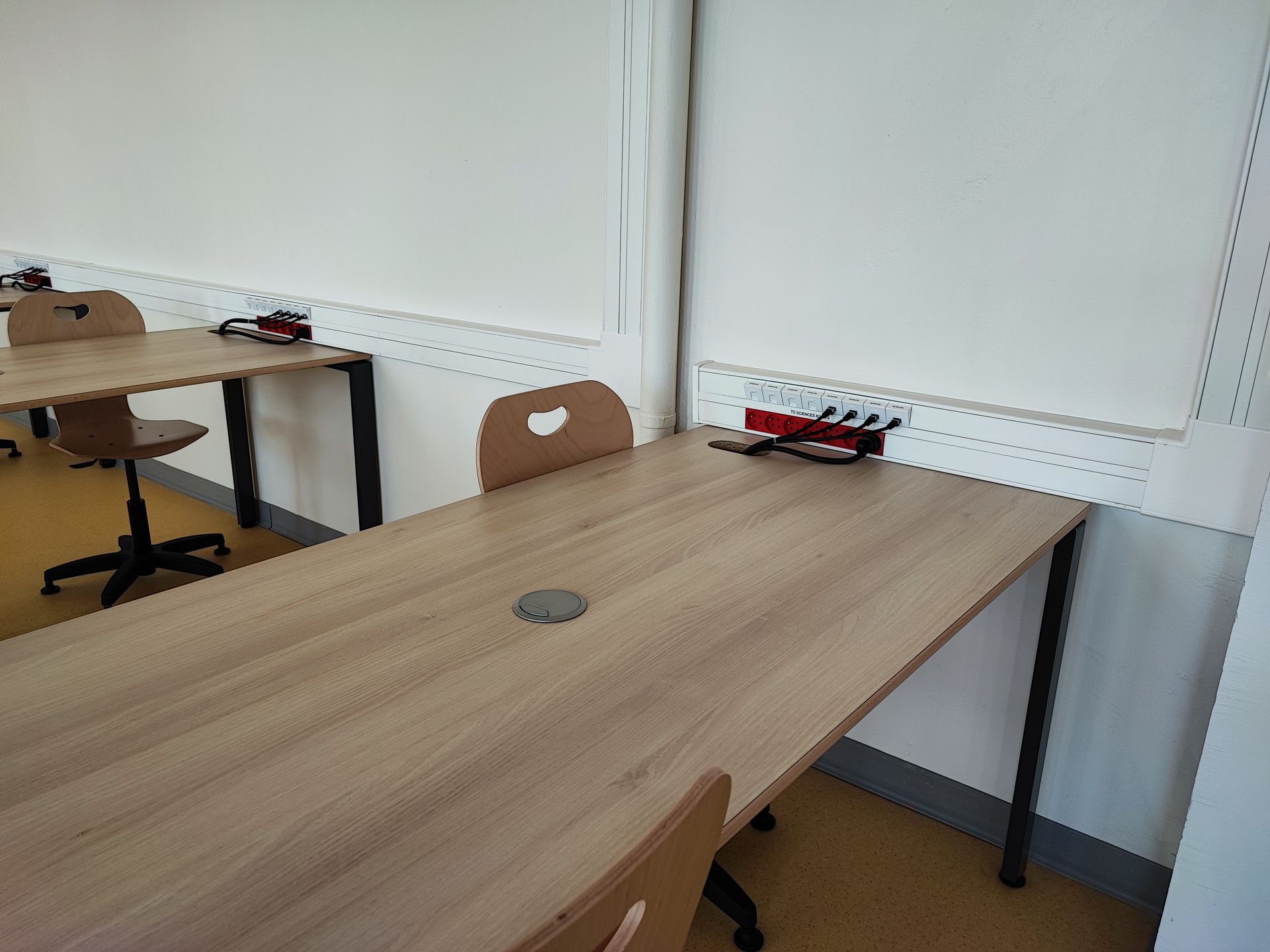 Une buanderie lumineuse et carrelée, avec une rangée de machines à laver, une table pliante en métal et de grandes fenêtres.