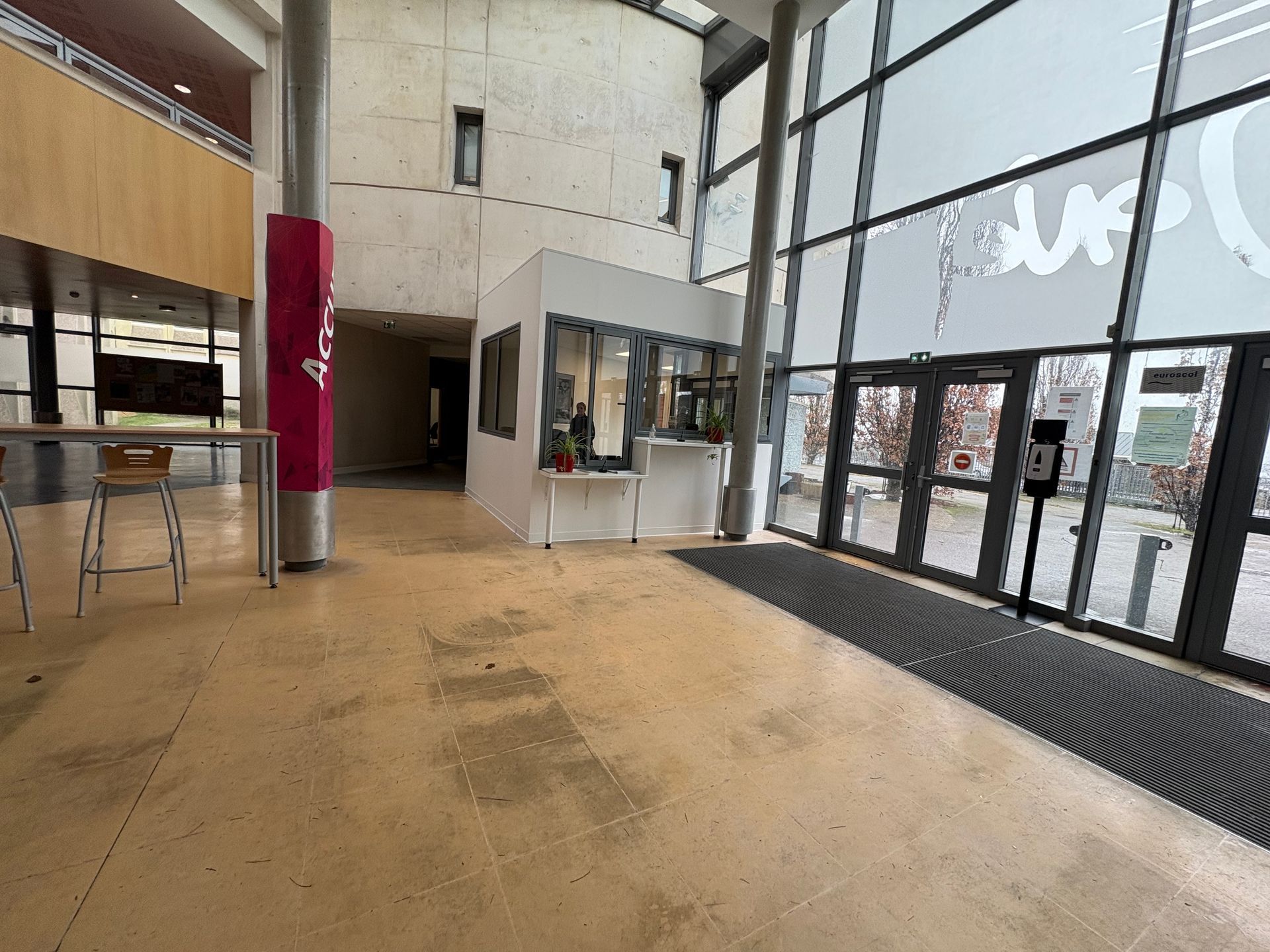 Hall d'entrée spacieux avec sol clair, portes d'entrée vitrées, bureau d'accueil et hauts plafonds.