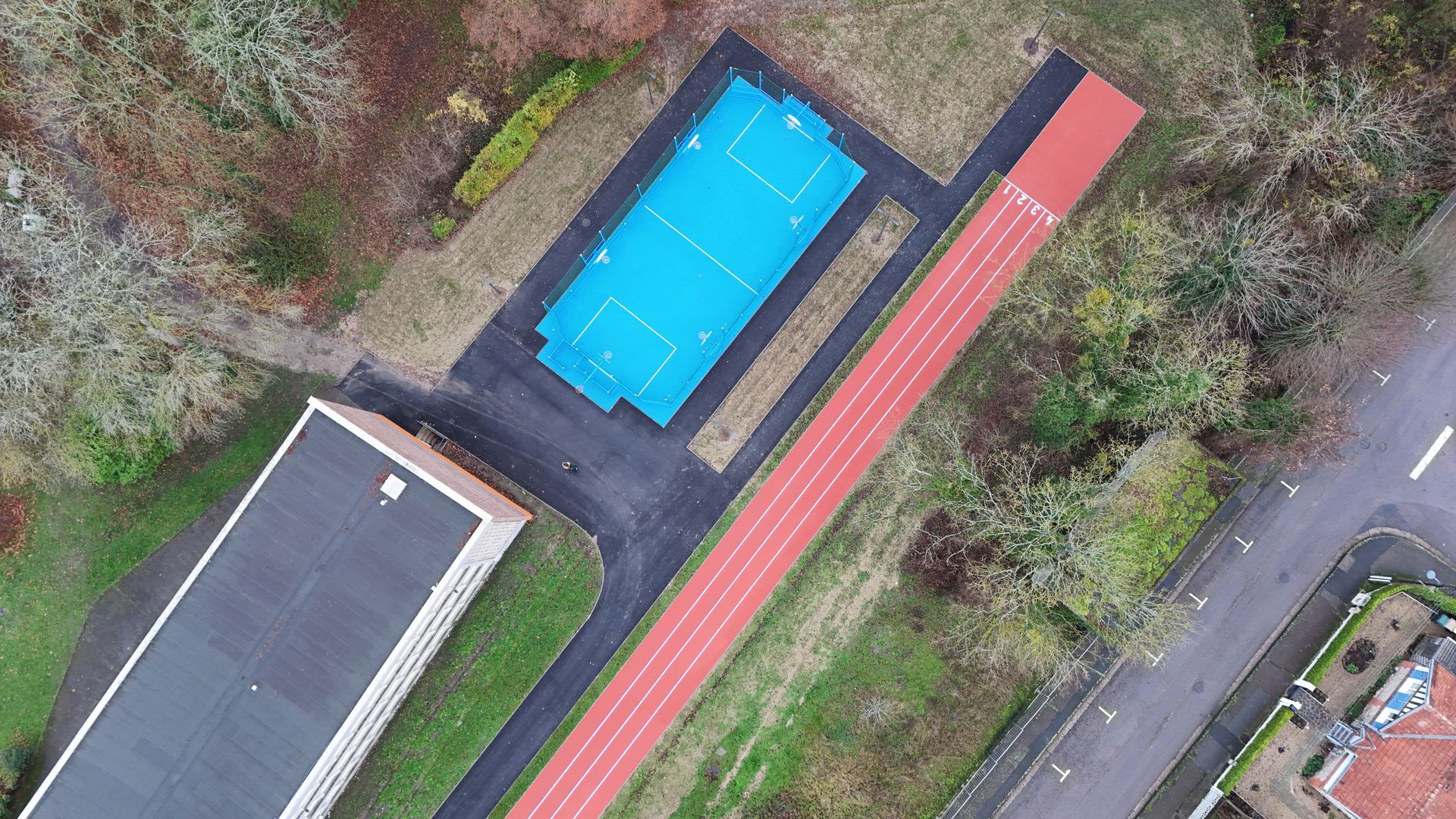 Vue aérienne d'une cour d'école montrant un terrain de sport rectangulaire bleu, une piste d'athlétisme rouge et un bâtiment.