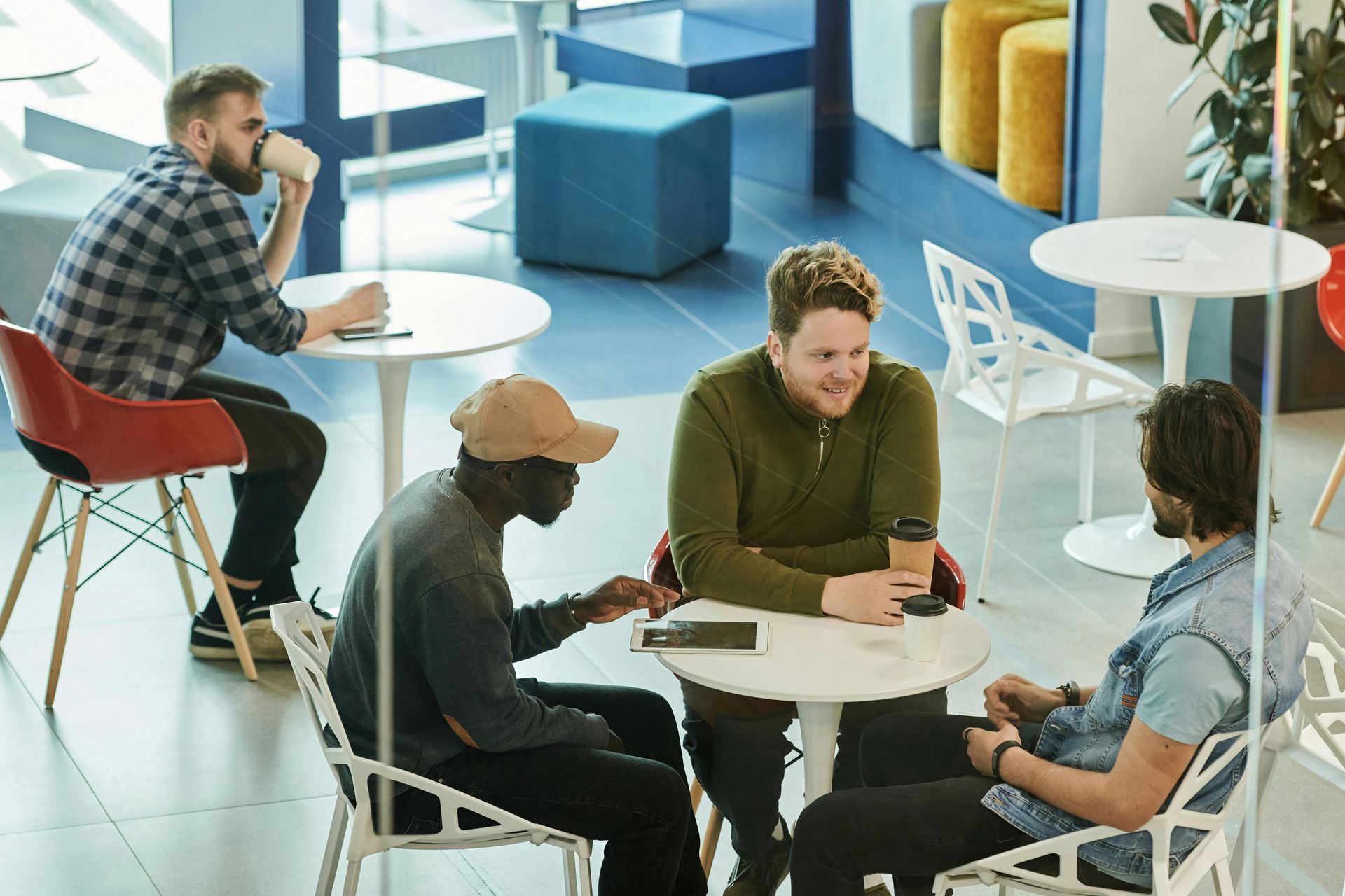 Dans un espace lounge moderne et lumineux, des personnes sont assises à de petites tables ; certaines travaillent, d'autres discutent en buvant un café.