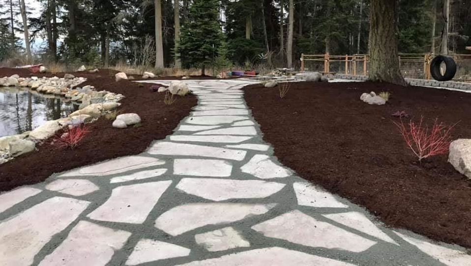 Flagstone path through a landscaped yard with a pond, trees, and dark mulch.