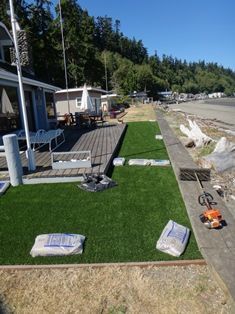 Artificial turf being installed on a waterfront deck. Bags of material and tools are visible.