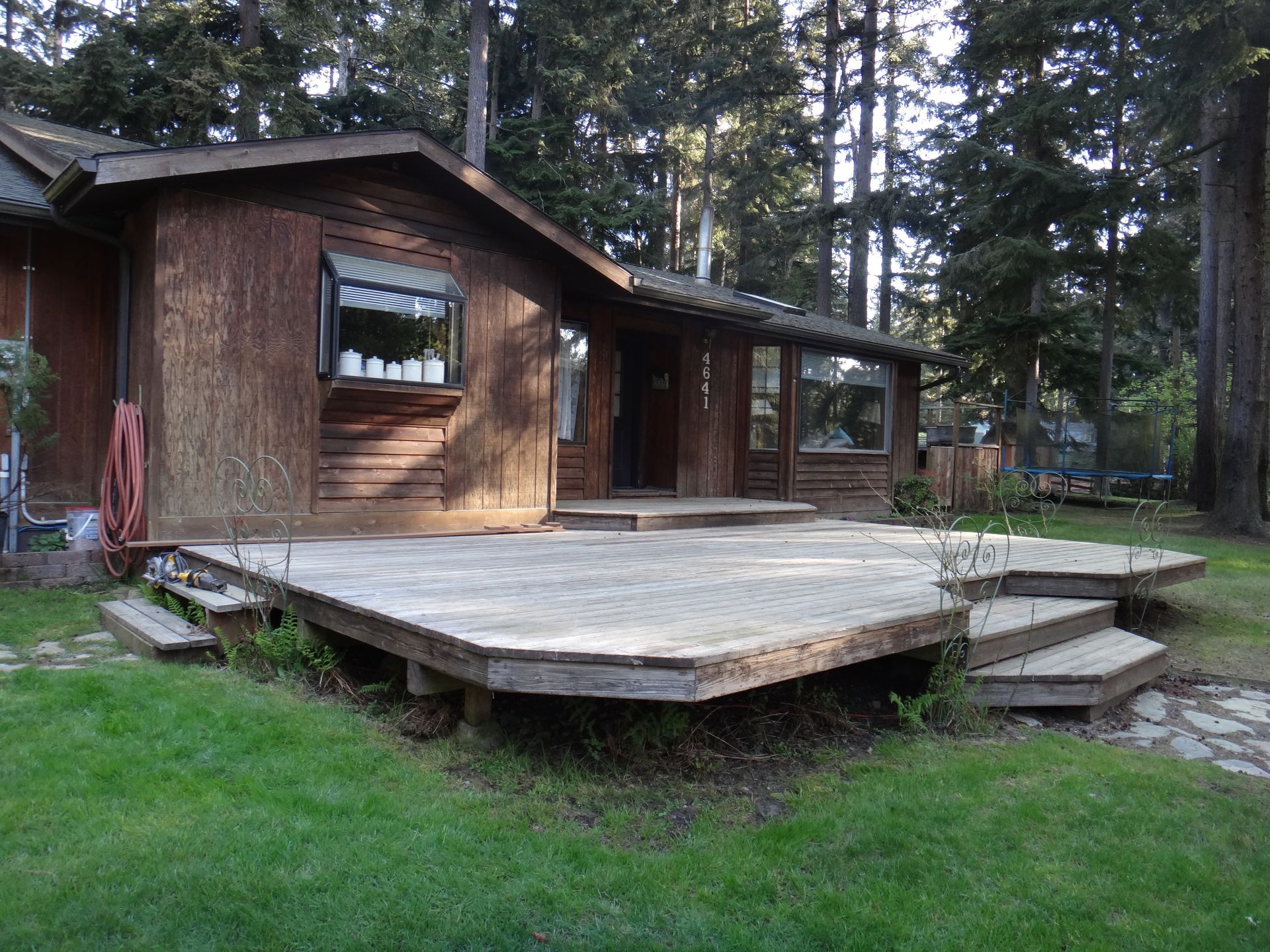 Wooden house with a weathered deck, surrounded by green grass and trees.