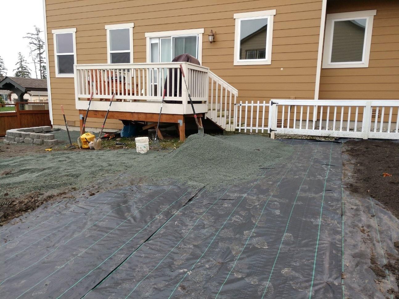 Backyard with a deck, gravel, landscaping fabric, and a brown house.