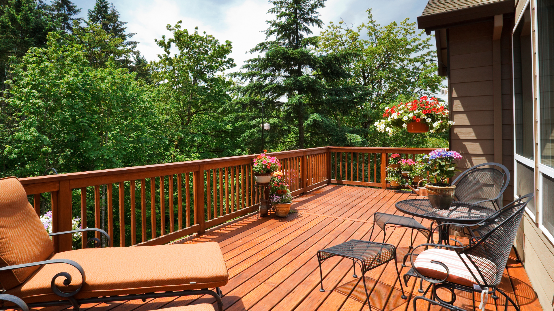 Wooden deck overlooking lush green trees, with patio furniture and potted flowers.