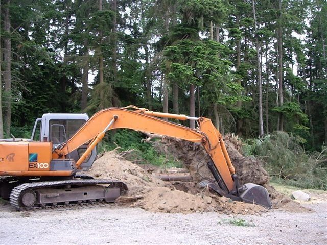Orange excavator digging dirt in a wooded area.