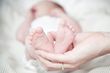 Hand cradles a newborn's tiny feet, skin is pink, baby is on white bedding.