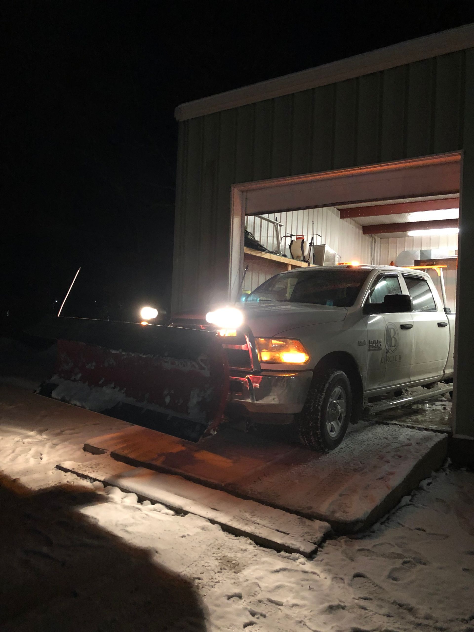 Pickup truck stuck in snow at a garage doorway at night, headlights on