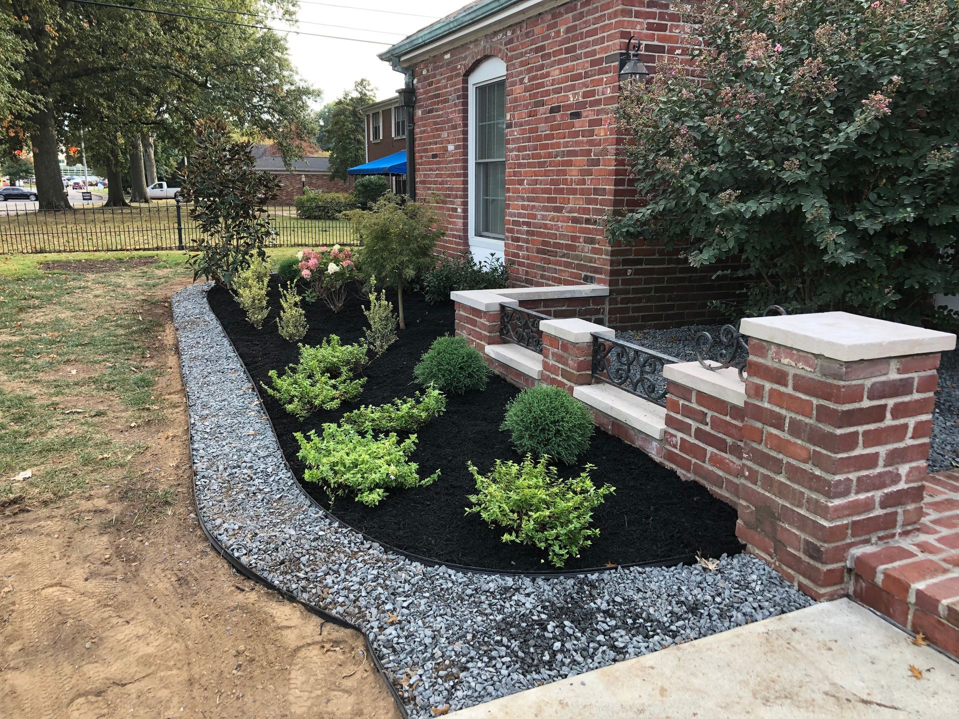 Landscaped brick house side yard with black mulch, shrubs, and a gravel border along a walkway